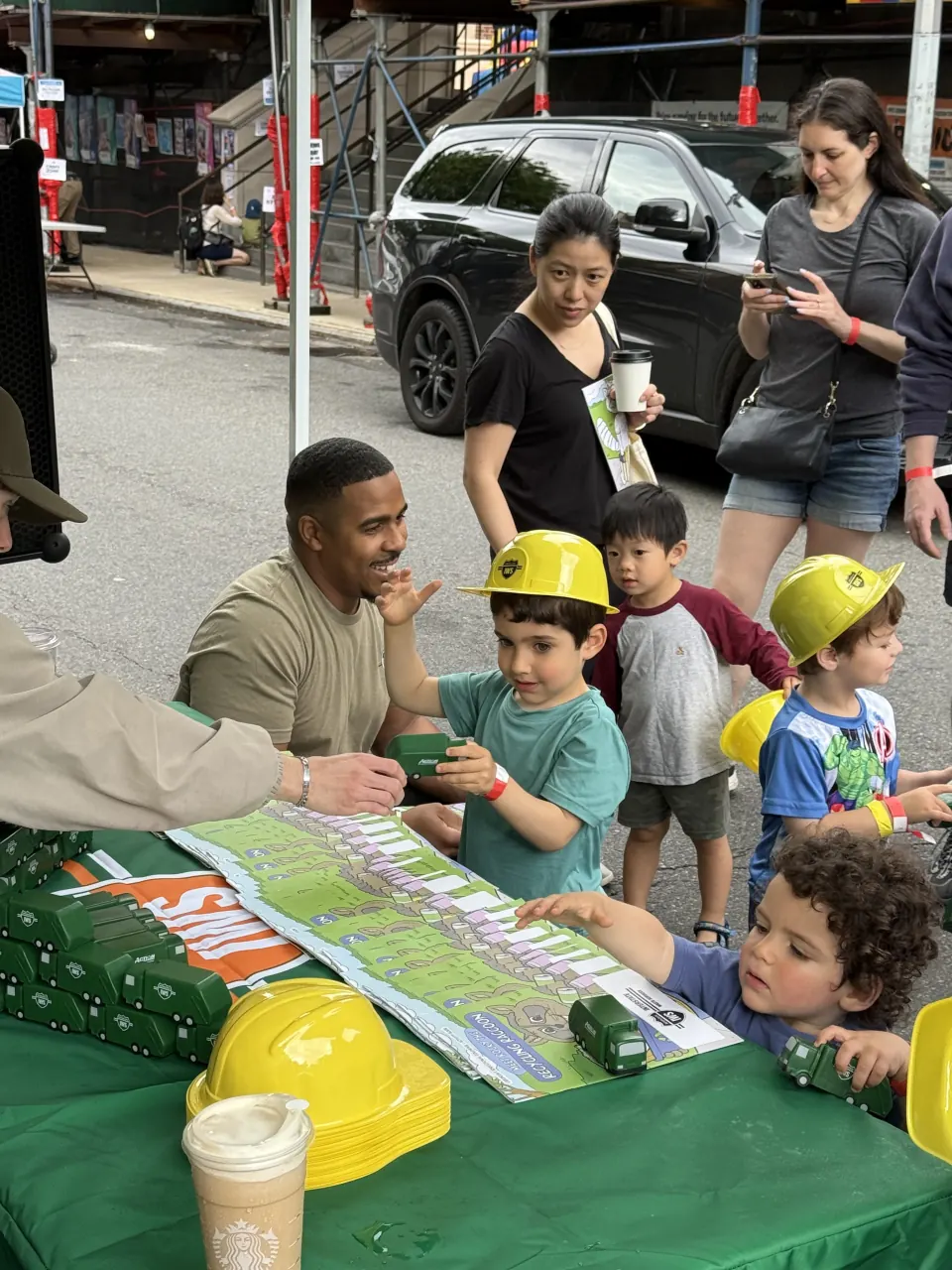 Children wearing Action hard hats playing with toy collection trucks at a New York City street event