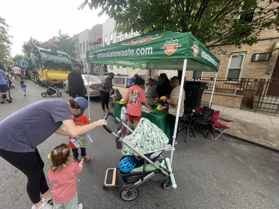 Families gathered at a neighborhood street event beside a branded outreach tent and collection trucks