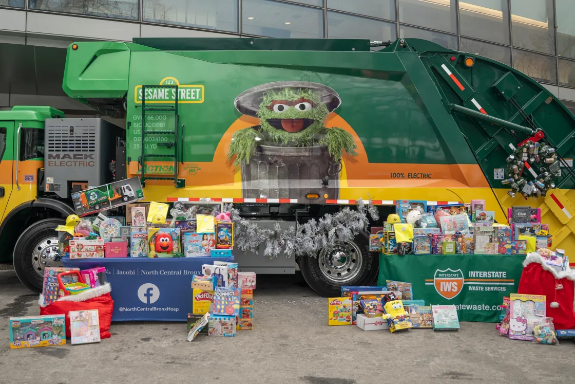 Donated toys collected for a holiday toy drive displayed in front of an Action Sesame Street electric collection truck