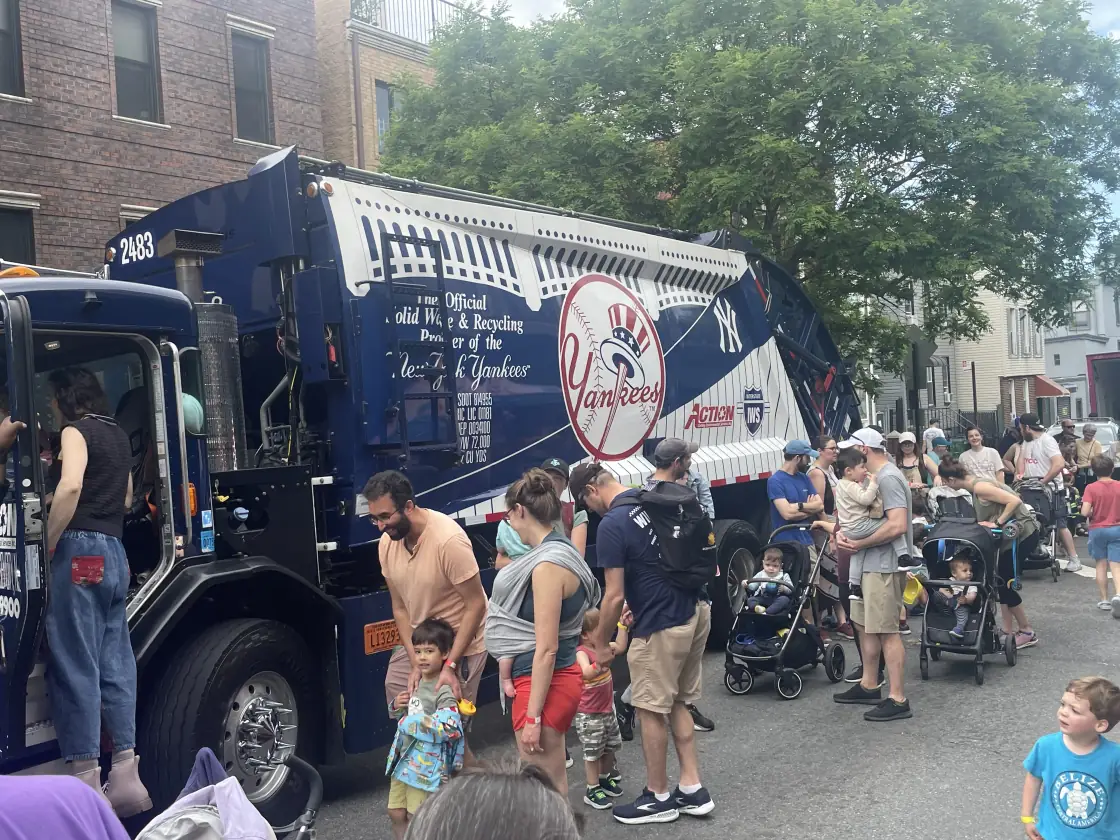 Families and children gathered around an Action New York Yankees collection truck at a neighborhood Touch-A-Truck event